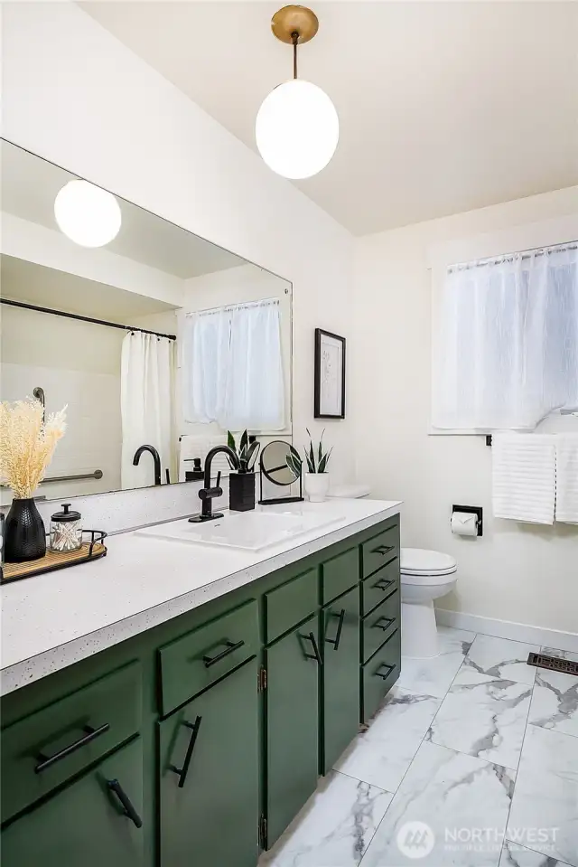 Main floor guest bathroom with plenty of space. Features new LVP flooring, updated faucet, newer sink, original solid wood cabinets painted forest green with new hardware, classic counters, tub/shower, and lighting