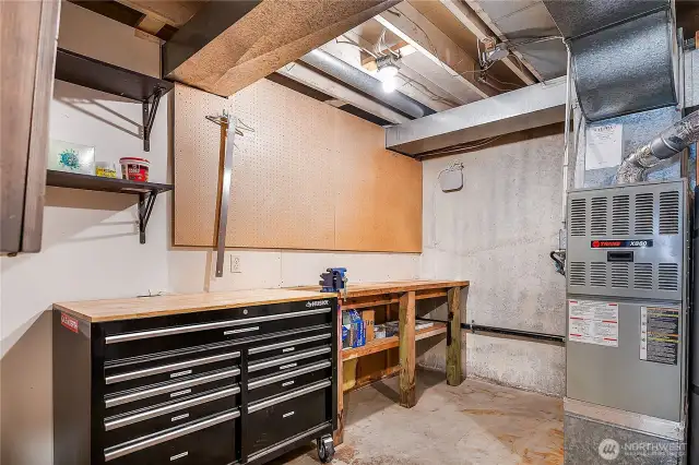 Downstairs furnace room has a shop area with built-in work bench, peg board, and shelving. To the right of the furnace there is even more space for storage. The furnace is made by Trane who is well known for making high-quality, long-lasting equipment.