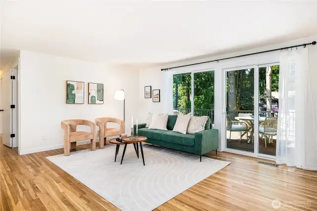 Main-level living room view looking toward the hallway and deck. Showcasing gleaming, refinished original hardwood floors that add warmth and character.