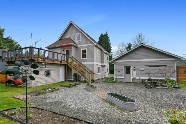 The back of the home with raised deck off the kitchen, storage under the deck for garden supplies and rear of the garage with man door entrance.