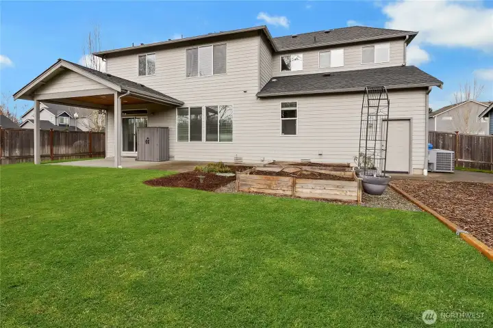 Back yard features raised garden beds and covered patio.