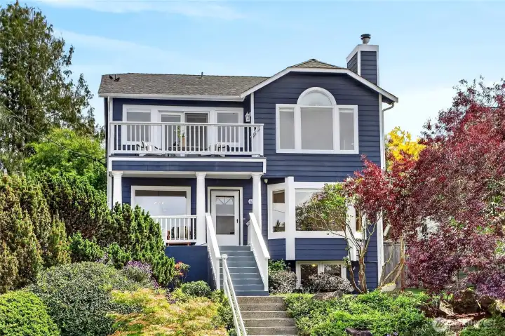 Storybook Northwest retreat with rich blue siding, vibrant mature gardens, sunlit balcony spaces, and timeless Pacific Northwest curb appeal.