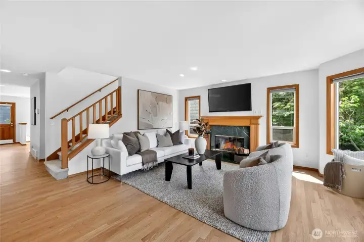 Inviting living room with warm hardwood floors, oversized windows, cozy fireplace, and bright open spaces designed for comfort and connection.
