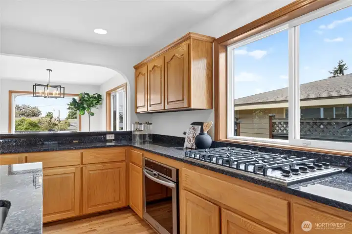 Sunlit chef’s kitchen with expansive prep space, gas cooktop, rich wood cabinetry, and oversized windows bringing in natural light.