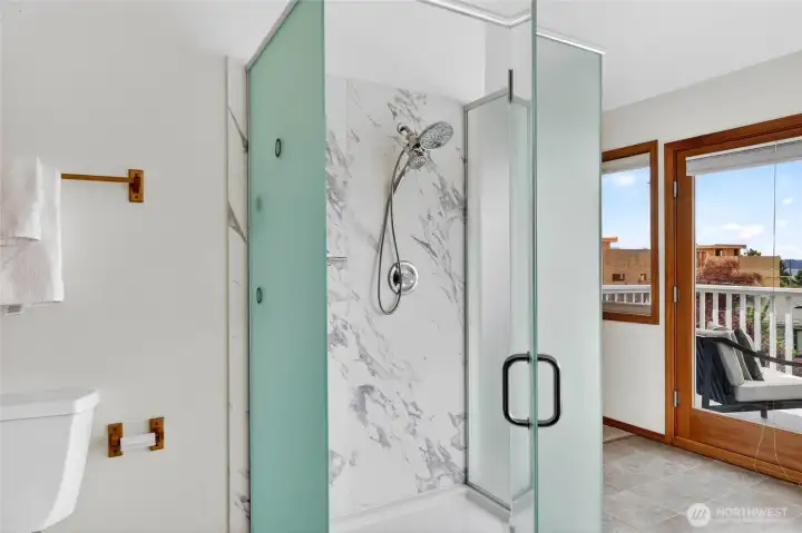 Elegant walk-in shower with sleek glass enclosure, marble-inspired finishes, and spa-like design beside private balcony views.