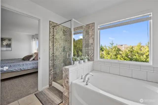 Primary bathroom with updated shower tile, spacious tub, and plenty of natural light.  The large picture window adds to the organic feel of this space.