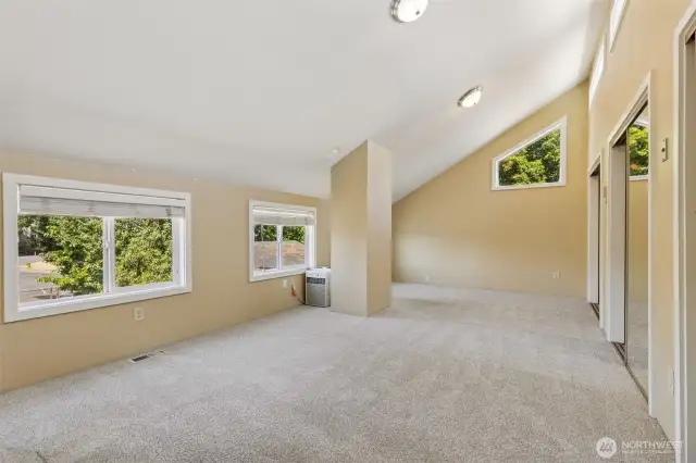Upstairs in Unit A, this massive vaulted room is a blank canvas for whatever you envision. With oatmeal carpeting and warm-toned walls, it’s a cozy yet spacious area. A big window with wide slat blinds, along with an upper accent window in the vaulted area, fills the room with light. Three huge walk-in closets give you all the storage you need, and the space is large enough to fit multiple sleeping dorm-style bunks or serve as a massive rec room for gatherings. At the end of the upstairs room in Unit A, the open loft space overlooks the staircase, adding a sense of openness and light. A deep walk-in closet at the top of the staircase offers extra storage, while the carpeted stairs ensure safety, comfort, and a quieter feel. The mirrored closet door reflects light, making the space feel even more spacious and bright.
