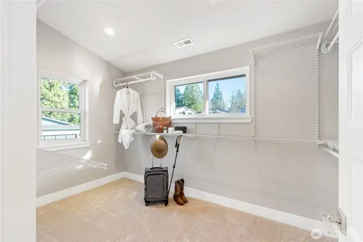 Huge walk-in closet with two windows and built-in shelving and hangers.