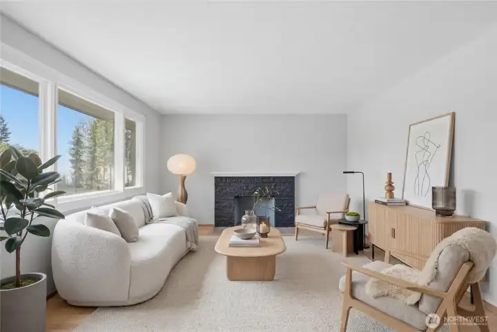 Virtually staged. Light-filled living room featuring hardwood floors, a charming fireplace, and expansive picture windows overlooking the mature landscape. Comfortable, functional, and ideal for everyday living and entertaining.