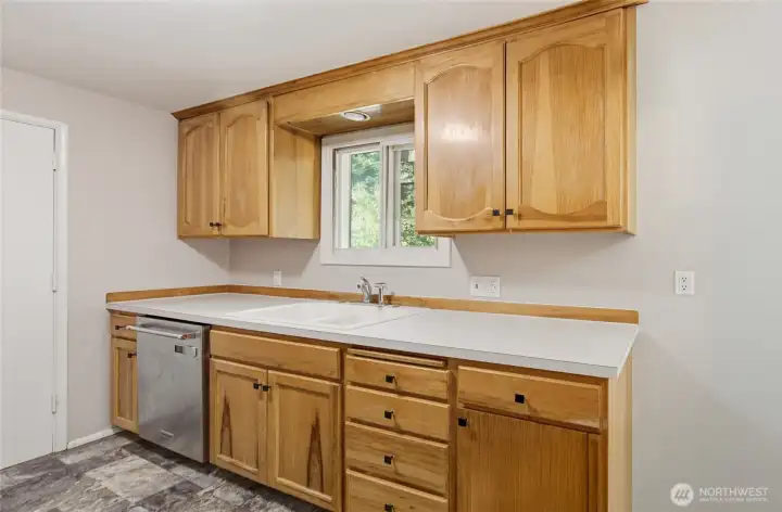 Functional galley kitchen featuring rich hickory cabinetry, generous counter space, updated appliances, and a window above the sink overlooking the backyard. Efficient design with ample storage and workspace for everyday cooking.