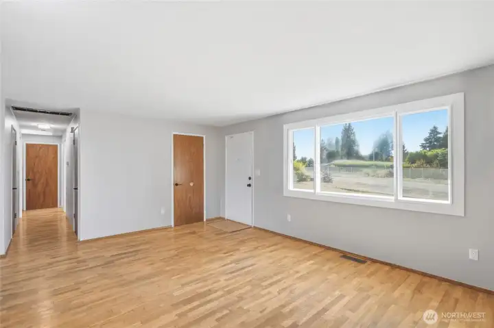 Light-filled living room showcasing beautiful hardwood floors, updated windows, and a functional layout that connects seamlessly to the bedroom wing and main living areas.