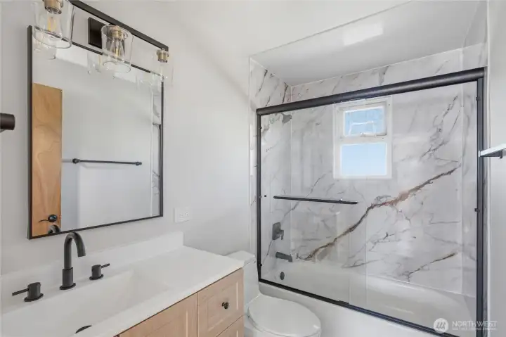 Fully renovated bathroom with custom tile surround, glass shower enclosure, modern vanity, matte black fixtures, and designer lighting. High-end finishes and thoughtful updates bring a luxury feel to this move-in ready SeaTac home.