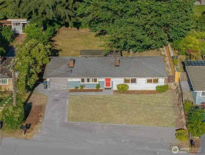 Aerial perspective showcasing this charming SeaTac rambler on a spacious 8,296 sq ft lot with a large backyard, mature trees, attached garage, and covered patio. Ideally located near Angle Lake, Link Light Rail, SeaTac Airport, parks, shopping, and dining.