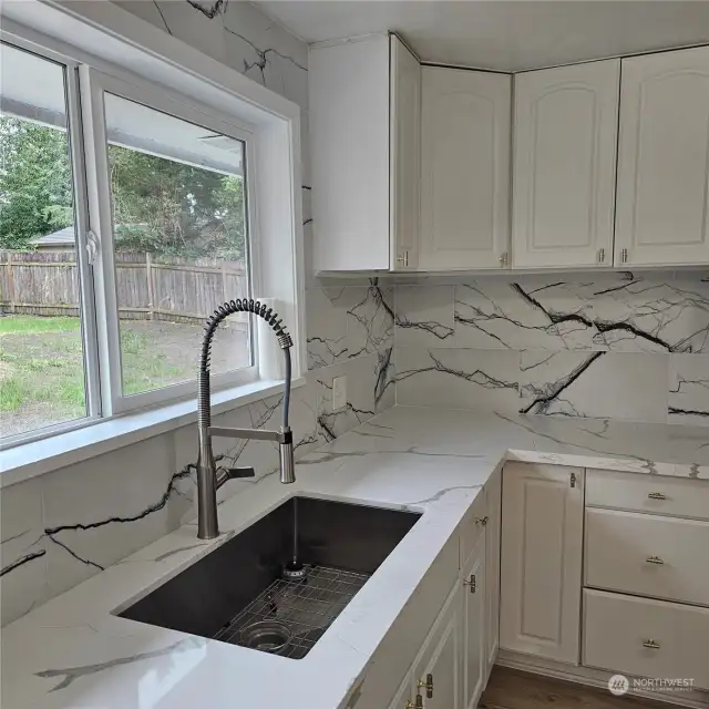 Very functional farm sink with quartz tile backsplash to cupboards