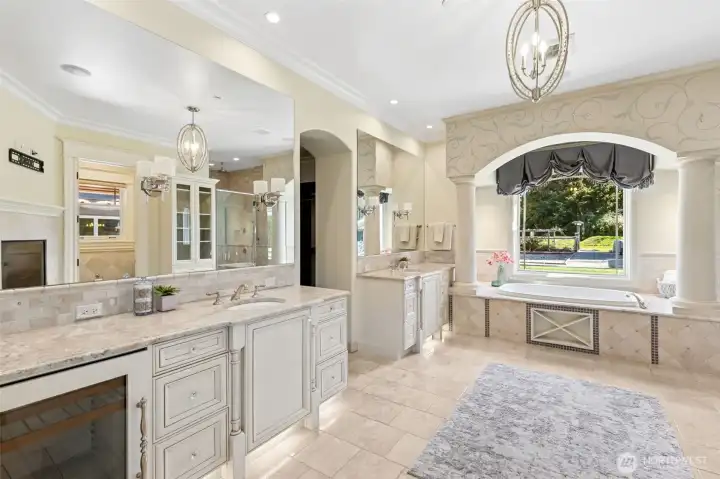 A luxurious, jetting tub offers private views of the side yard—perfect for relaxing. Beneath the mirrored cabinet, a discreet fridge provides convenient storage for your skincare, medications, or even a chilled glass of champagne to savor during a soothing bubble bath before bedtime.