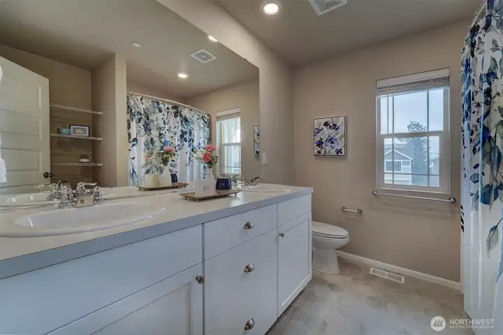 Guest bathroom has double vanity, shower/tub combo, and built-in linen storage.