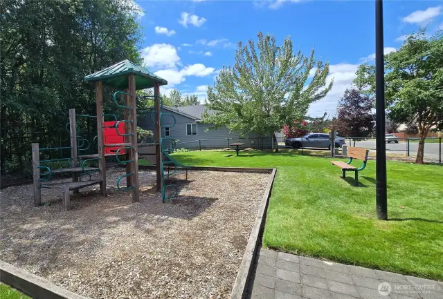 Fenced park with climber, bench, picnic table and basketball hoop.