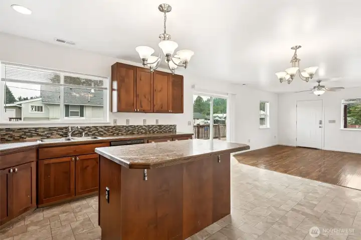 Looking across the kitchen, you get the full effect, with a no-fuss neutral Formica countertop on the island with a corner-clipped design to avoid any head-bonking from kids doing laps. The big window over the sink, the dining area with its chandelier, the sliding glass door to the deck, even the front door and living room windows all line up to show the great room flow.