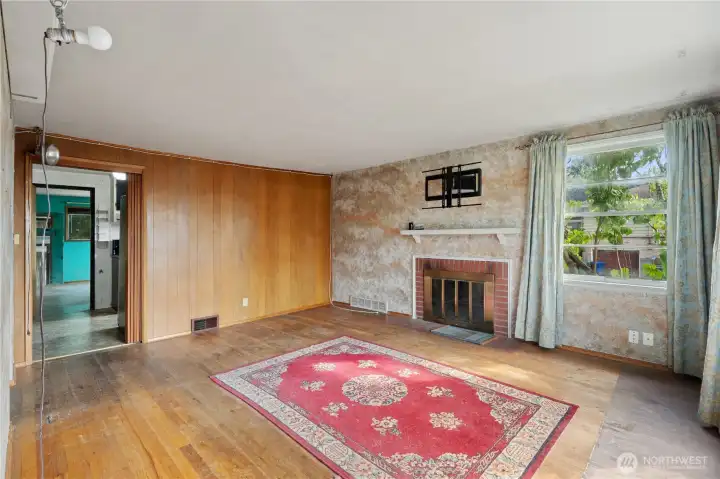 Living room with original hardwood flooring, wood-burning fireplace and wood-paneling details.