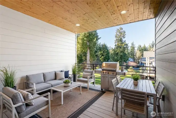 Covered outdoor living deck with natural stained wood soffits right off of the kitchen for easy access for your morning coffee, or BBQ nights. Custom metal railing, conveniently plumbed with water and electric outlets.