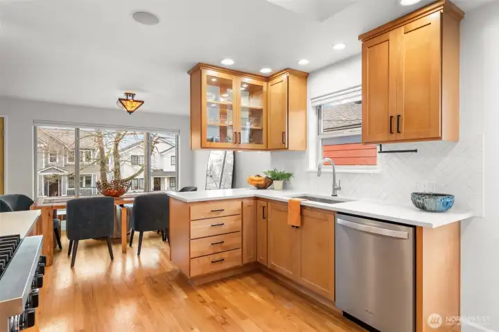 Light-filled corner kitchen featuring quartz countertops, stainless appliances, and a modern herringbone backsplash. Thoughtful cabinetry and clean lines deliver both storage efficiency and architectural presence.
