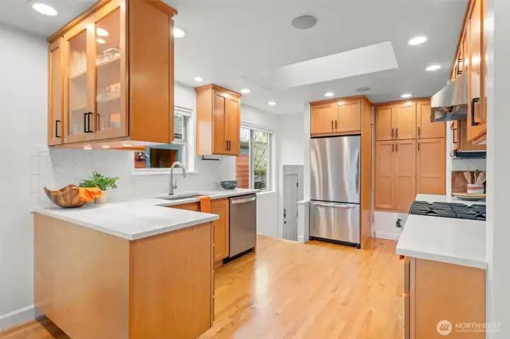 Generous prep areas, stainless refrigerator, and abundant custom cabinetry create a kitchen built for serious cooking. Skylight and recessed lighting enhance brightness and elevate the overall design experience.