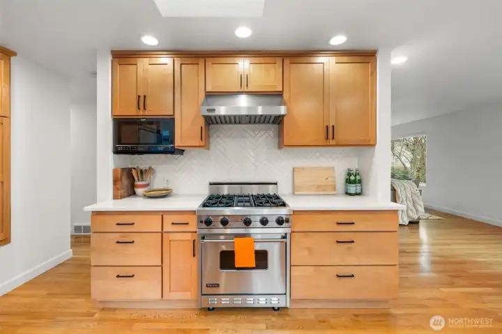 Professional-grade Viking gas range with commercial hood anchors this chef-caliber kitchen. A striking herringbone tile backsplash, custom cabinetry, and quartz counters elevate both design presence and culinary performance