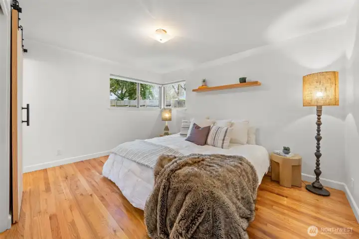 Welcome to the Primary Suite featuring hardwood floors, clean architectural lines, and a sliding barn door detail that adds modern character. Corner windows introduce natural light while maintaining privacy and tranquility.