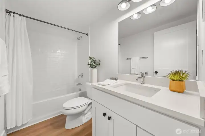 Lower-level main bathroom featuring a full tub with subway tile surround, quartz vanity, and modern fixtures