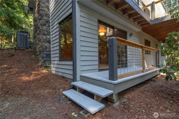 This photo shows the efficient heat pump on the left, brand new deck railings up & down, and this corner room is the lower level family room with a wood fireplace.
