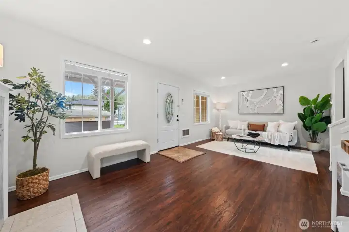 A bright, welcoming entry flows seamlessly into the living room, showcasing rich hardwood floors, recessed lighting, and an abundance of natural light through picture windows. The open layout makes it easy to personalize the space for everyday comfort or effortless entertaining.
