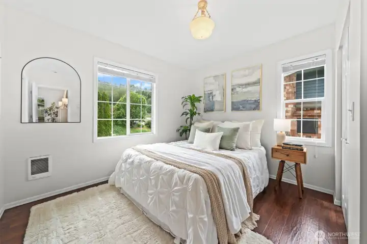 Wake up in this bright and airy, main level Primary Suite 1 filled in natural light from dual windows overlooking lush greenery. Rich hardwood floors, a charming pendant light fixture, and a calm, neutral palette create a peaceful retreat you'll look forward to coming home to.