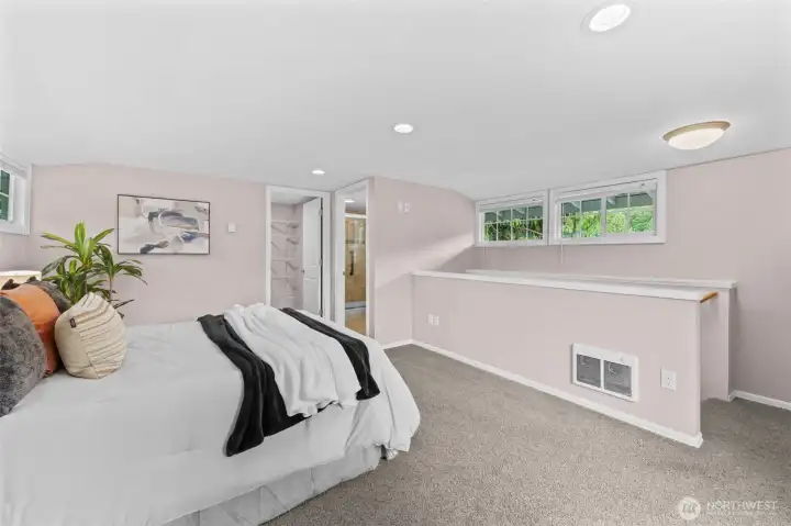 The expansive layout of the upstairs Primary Suite 2 allows for a full sitting or lounge area, with windows on multiple sides bringing in greenery views and natural light. A private ensuite bath is visible through the doorway, completing this comfortable and functional retreat.