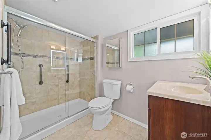 Primary Suite 2 bath features a full-height tile walk-in shower with sliding glass enclosure, a rich cherry vanity with granite countertop, and a bright frosted window for privacy with natural light. Clean lines and quality finishes make this a refreshing space to start and end your day.