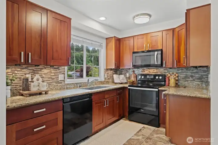 Generous counter space, full-height cherry cabinetry, granite countertops, and a stone mosaic backsplash make this kitchen both beautiful and practical. The Whirlpool appliance suite — including a range, dishwasher, and over-the-range microwave — is ready for everyday cooking and weekend meal prep alike.