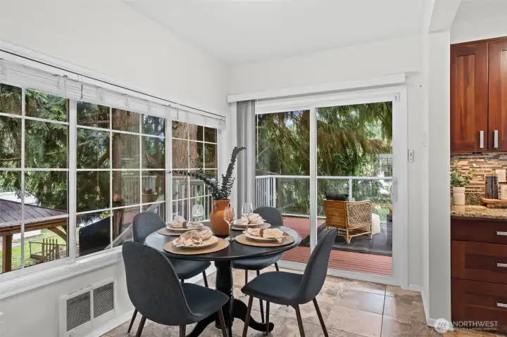 You'll love this sun-drenched breakfast nook wrapped in windows on two sides, overlooking the river, deck and lush greenery beyond. The sliding glass door provides direct access to the outdoor living space, making al fresco dining effortless any time of year.