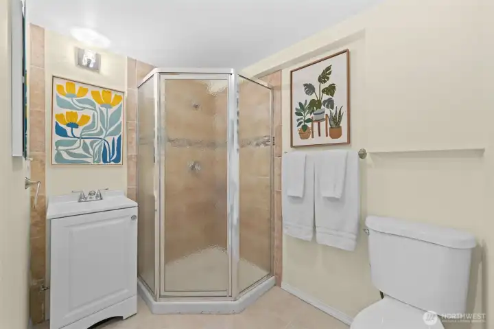 This lower level bath features a corner glass-enclosed shower with tile surround, a pedestal vanity, and a clean, functional layout that serves guests and the lower level living space equally well.