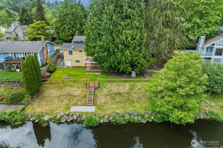Rare riverfront living in a sought-after neighborhood setting — this aerial view reveals the home's incredible positioning along the water with direct backyard access, lush mature trees, and a private staircase to the shoreline. You'll love having nature this close while still being minutes from everyday conveniences.