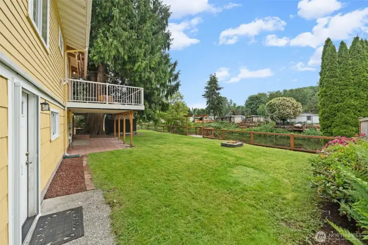 This generous, sun-filled backyard showcases a vibrant lawn, colorful perennial plantings, a built-in firepit, and a covered lower patio tucked beneath the elevated deck — giving you multiple distinct outdoor living spaces to enjoy year-round. The cedar fence with waterfront gate, upper deck views, and lush arborvitae border make this backyard as private as it is inviting.