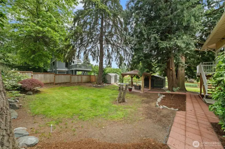 A beautifully established backyard retreat surrounded by towering evergreens and mature Japanese maple, with a level area, a covered cedar gazebo, a storage shed, and a charming paver patio perfect for outdoor dining and entertaining. The fully fenced yard offers privacy and room to play, garden, or simply unwind in a serene Pacific Northwest setting.