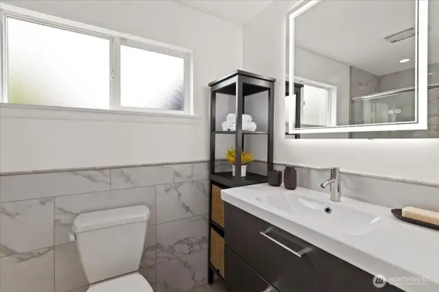 Marble-style tile, modern fixtures, and a backlit mirror elevate the ensuite bathroom experience.