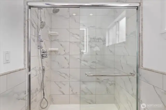 Marble-style tile, modern fixtures, and a backlit mirror elevate the ensuite bathroom experience.