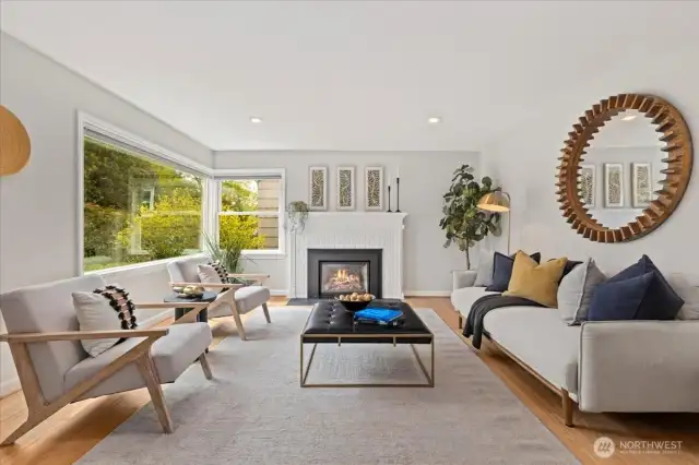 Expansive corner windows flood the space with natural light, complemented by a cozy gas fireplace and serene palette.