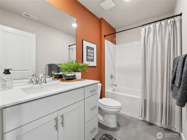Stylish secondary bath pairs a quartz-top vanity and full tub/shower combo with a bold terracotta accent wall for designer flair. Pictures are for representational purposes only, colors and features may vary