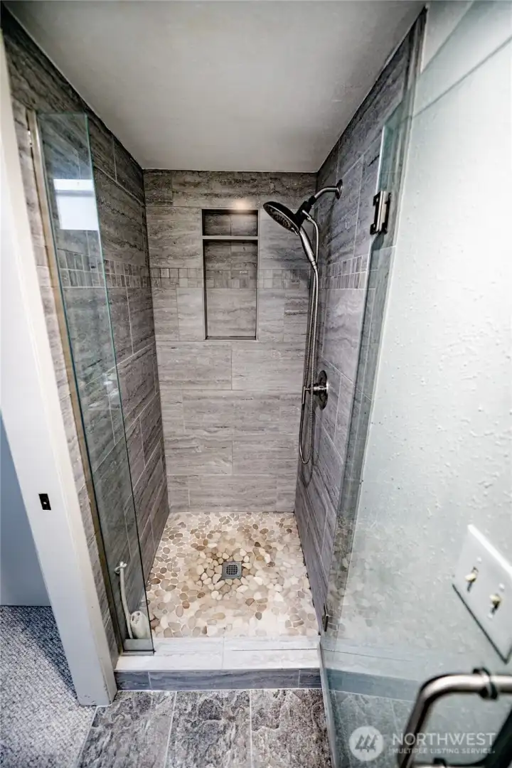 Newer porcelain tile on both floor and walls with glass door in primary bathroom.