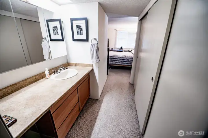 View from primary bathroom looking into bedroom. New vanity/sink and tri-mirror medicine cabinet. His/her closets to right.