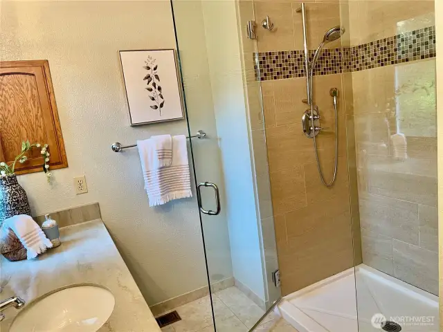 The primary bathroom shower is designed with a sleek, frameless glass door that enhances the space with an open, modern aesthetic.
