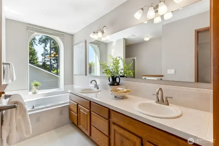 Updated 5-piece primary bath is like a spa retreat with double-sinks, large soaking tub, lots of cabinet space with stylish tile countertops and an arched window for that amazing natural light that this home has around every corner.