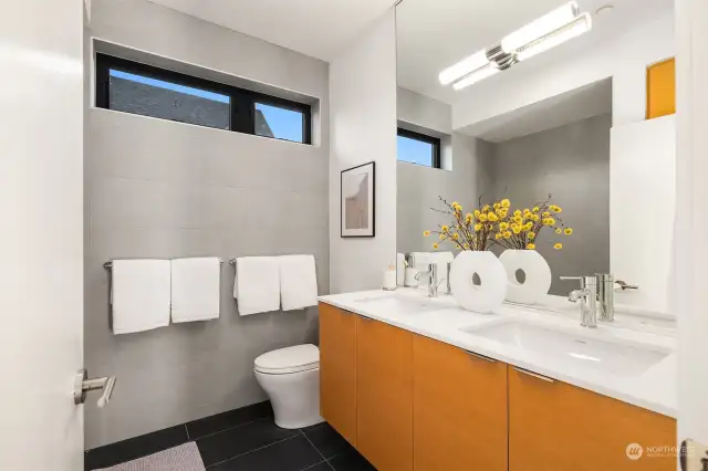 The bathroom maintains a consistent level of luxury including Abodian cabinetry, quartz countertops, ceramic tile floors, and Grohe WaterSense fixtures, reflecting a commitment to quality and sophistication that runs throughout the home.