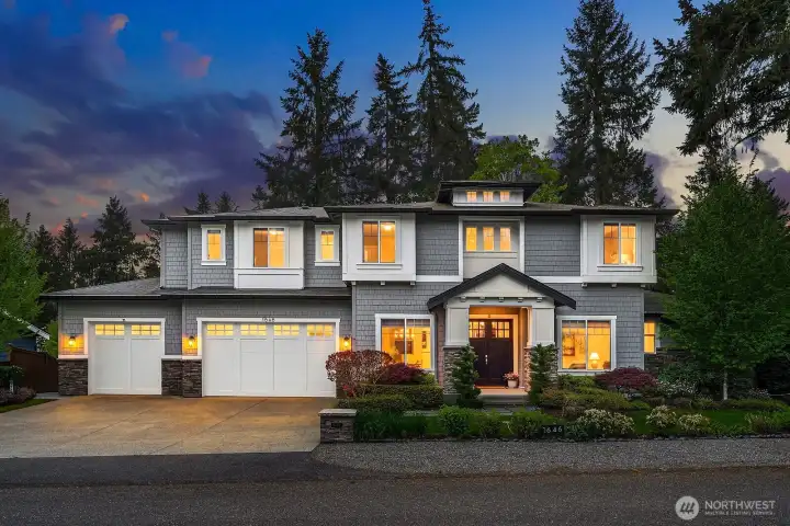 A stunning custom JayMarc craftsman showcasing impeccable curb appeal with a three-car garage, elegant stone accents, and vibrant professional landscaping — a grand and welcoming first impression in the heart of West Bellevue's coveted Enatai neighborhood.
